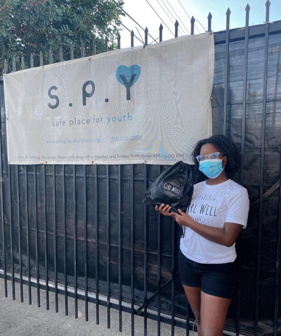 Girl holding a bag and posing next to a sign